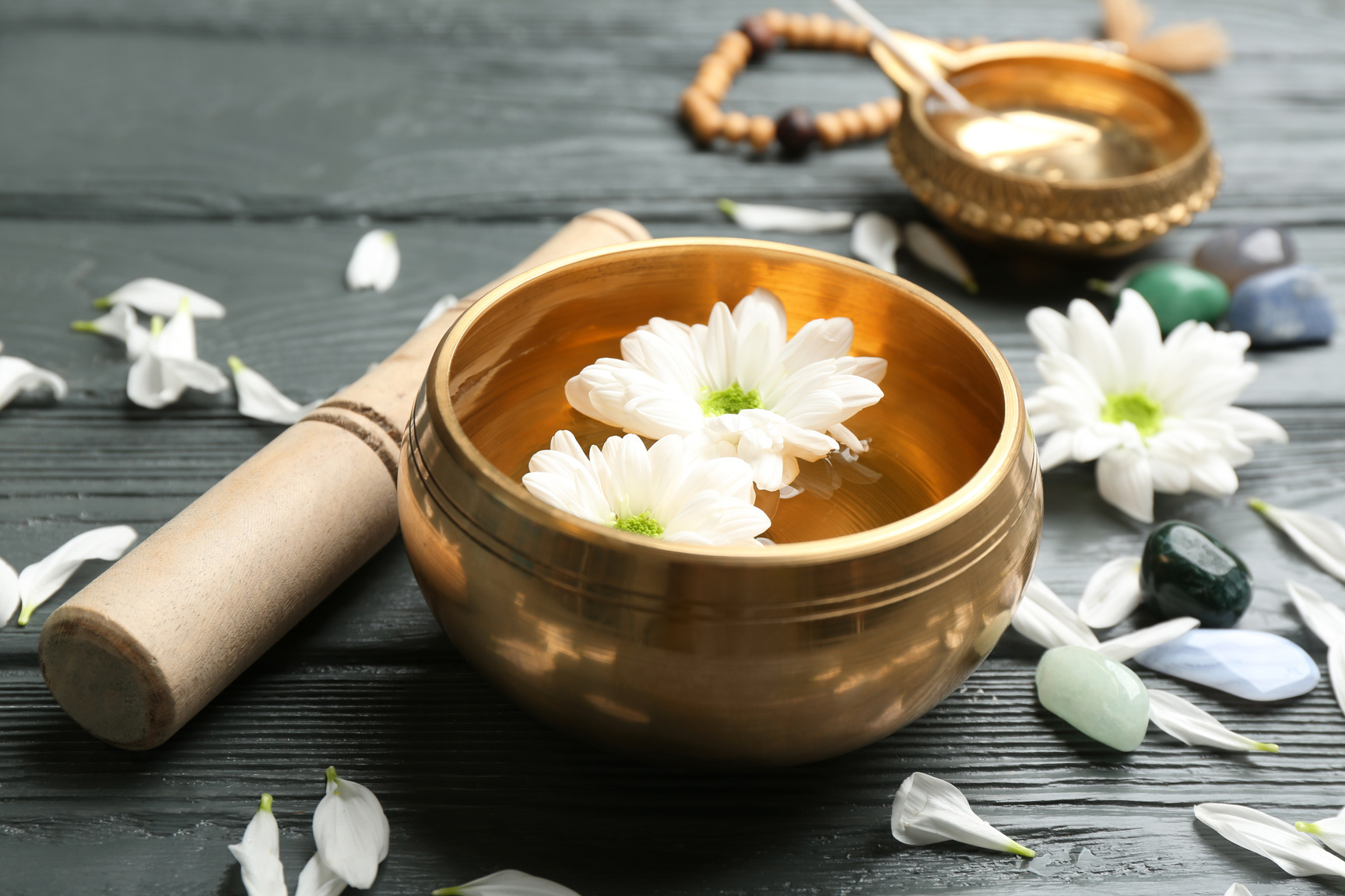Golden Singing Bowl with Flowers and Mallet on Grey Wooden Table, Closeup. Sound Healing